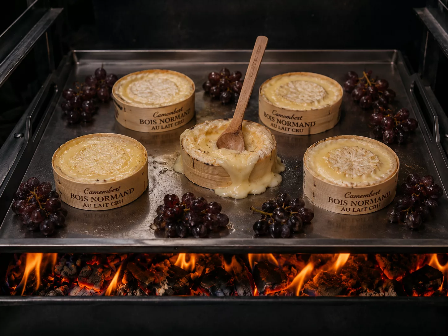 Camembert aus der Normandie auf der Griddleplatte auf Holzkohle erwärt wird mit gerösteten Weintrauben serviert.