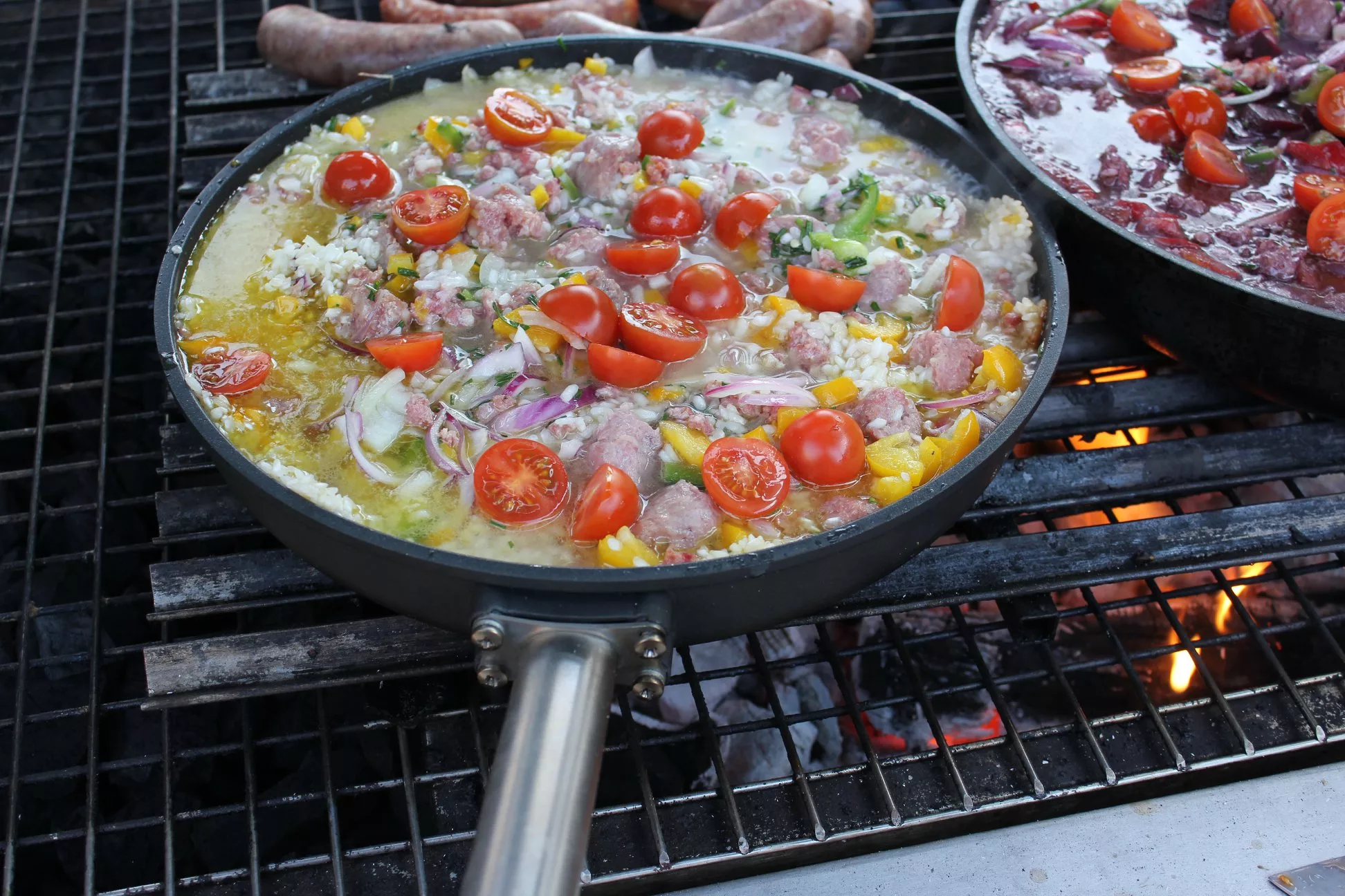 wir sehen eine große pfanne auf dem grill in der bester risotto frisch zubereitet wird, bunt und nur mit frischesten zutaten